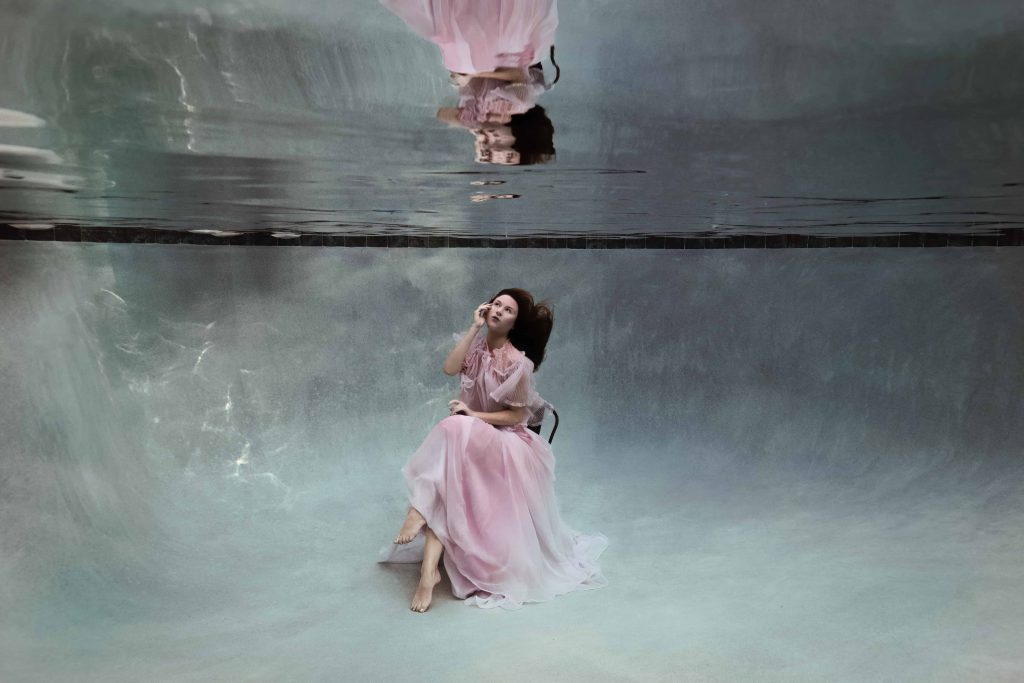 A woman is sitting on a chair underwater while wearing a pink ruffled skirt during her underwater photography session in Florida.