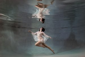 A woman wearing a sheer, lace kaftan dances while posing for her underwater photoshoot at our Jacksonville, Florida studio.