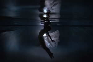 A woman wearing a sheer skirt floats underwater with a light shining behind her and through her skirt during her underwater portrait session.