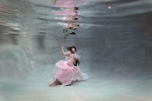 A woman wears a bumble gum pink skirt while sitting in a chair underwater during her photoshoot at our underwater studio in Jacksonville, Florida.