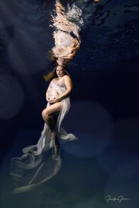 A pregnant mother wearing a sheer white dress floats underwater during her underwater maternity session in St. Augustine, Florida.